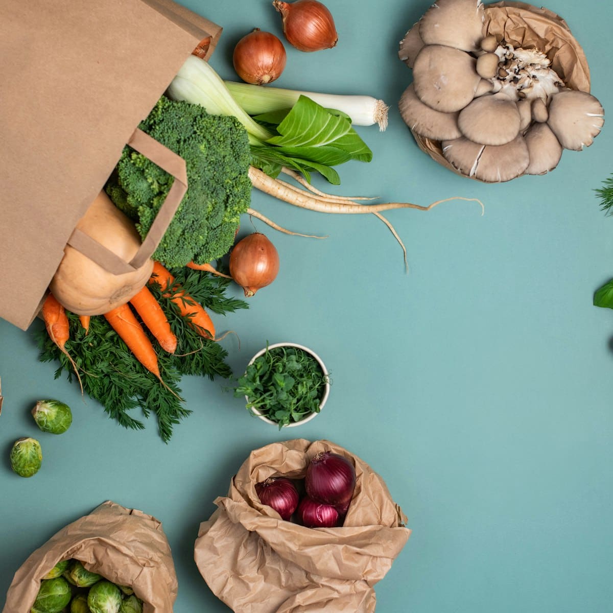 A paper grocery bag on its side with carrots, broccoli, onions and mushrooms spilling out