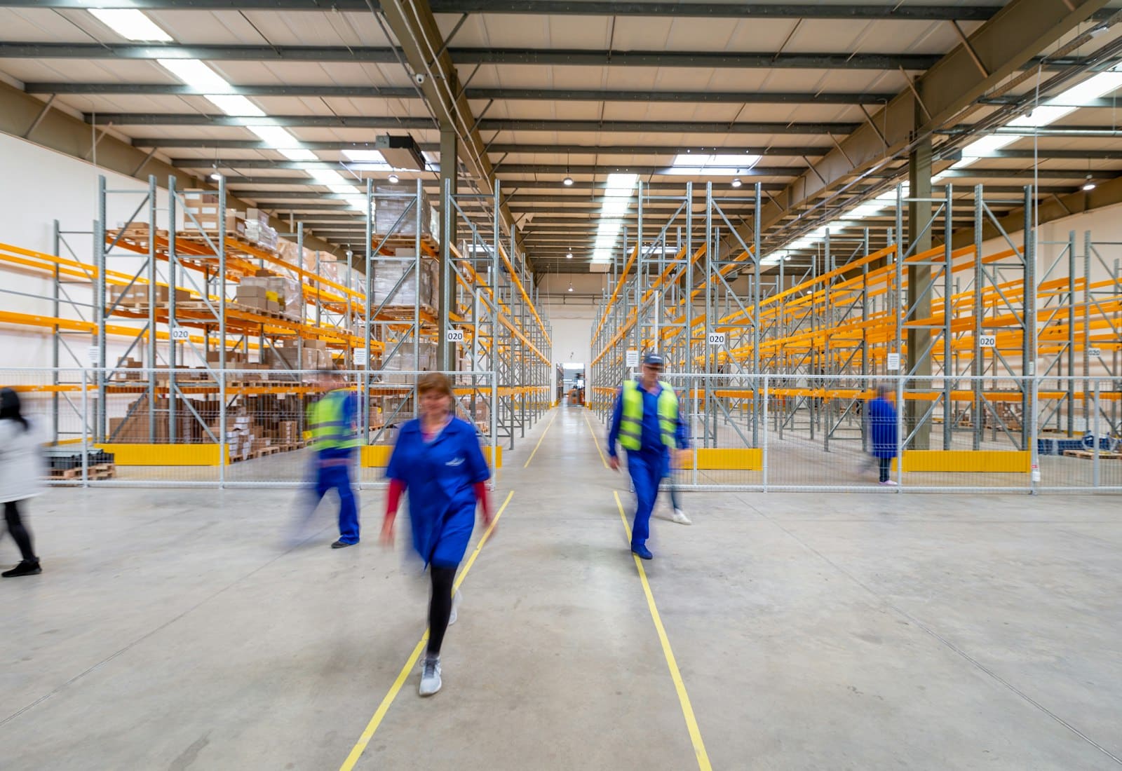 Staff walking a warehouse aisle between tall racking, caught mid-stride
