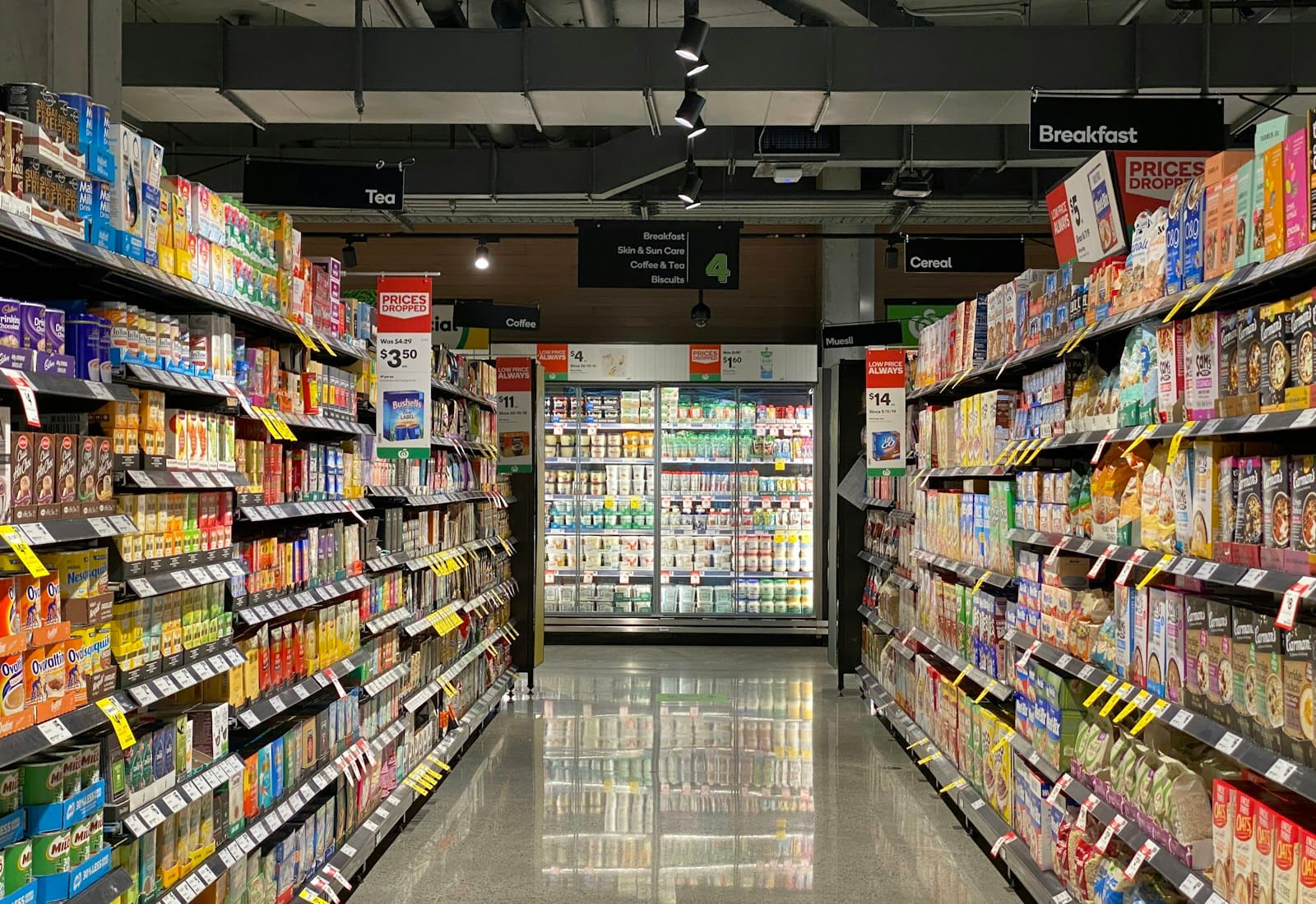 A brightly lit supermarket aisle photographed down its length, shelves stocked on both sides