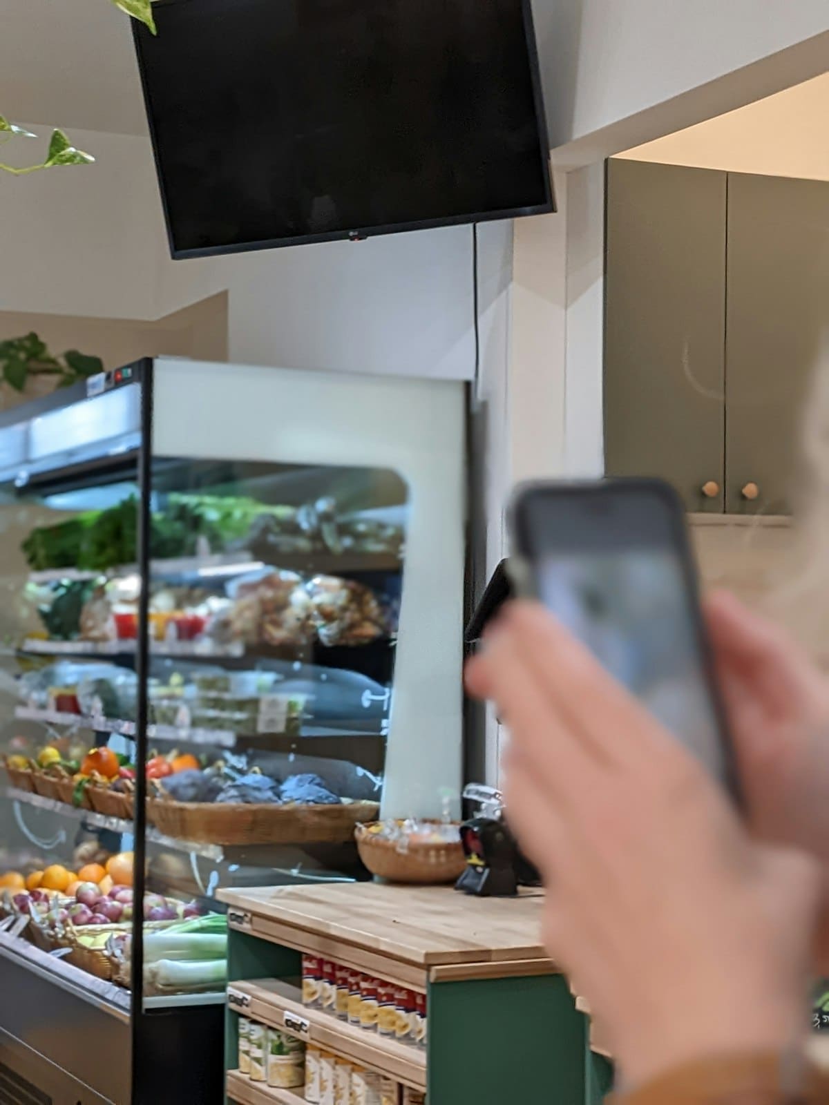 A customer holding a phone in front of a refrigerated fresh food display