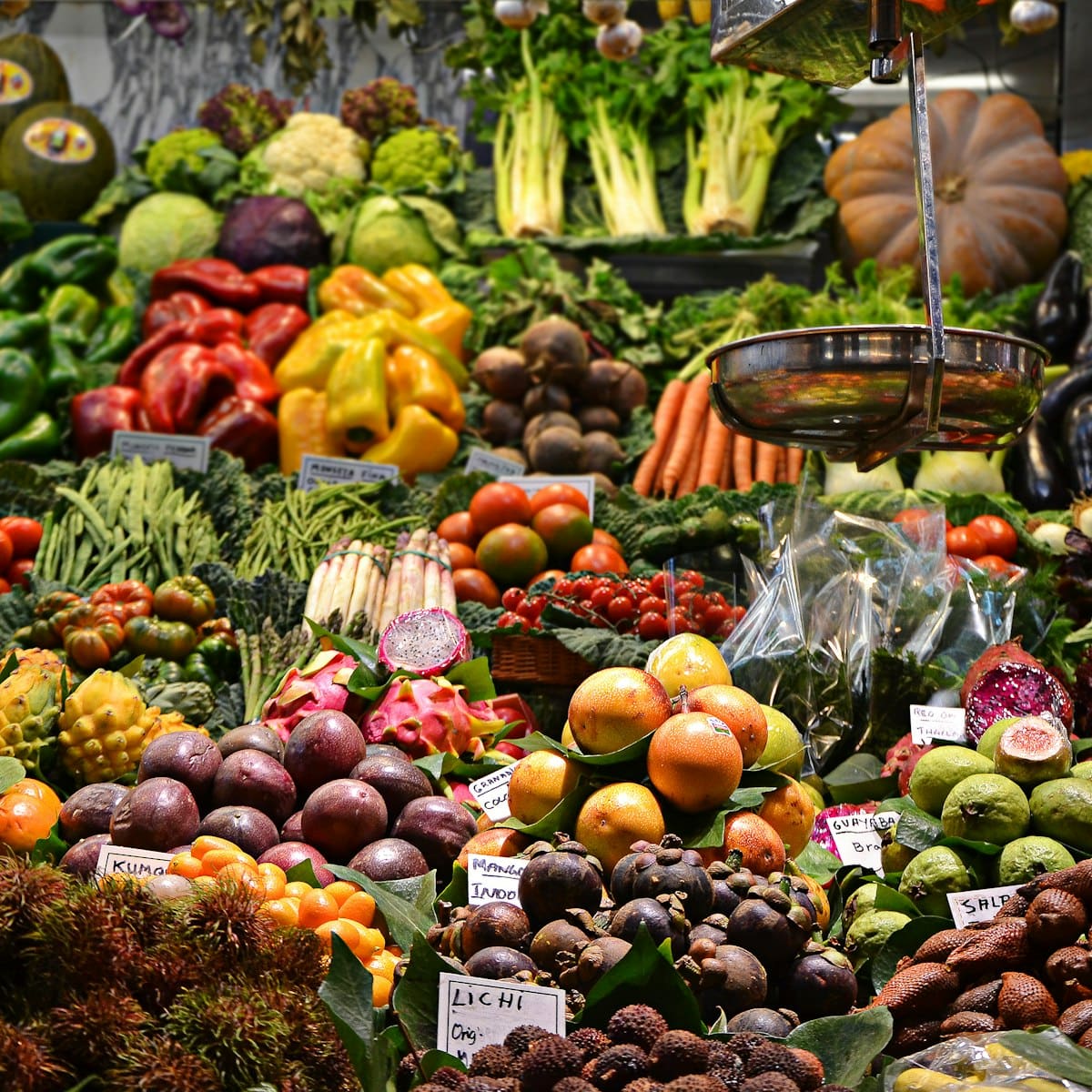 A market stall piled with oranges, apples, peppers and leafy greens