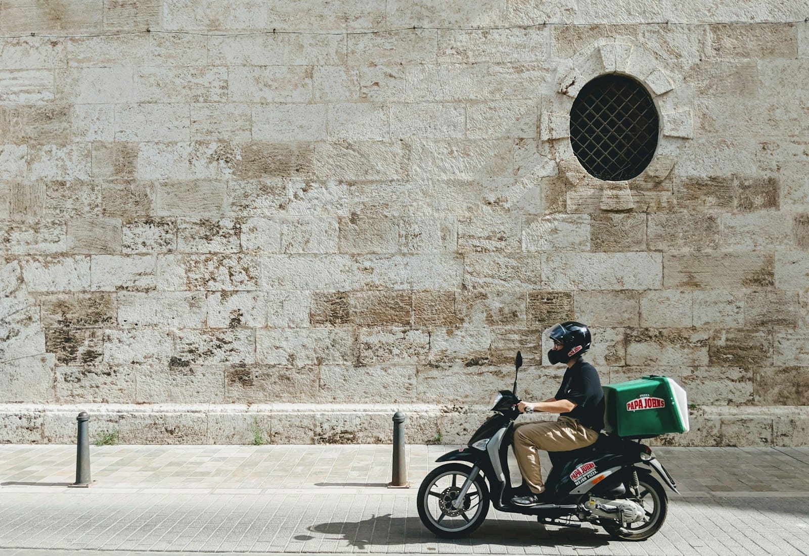 A delivery scooter with a cargo box parked against a bare wall