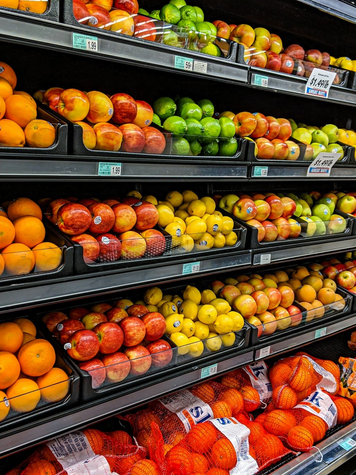 Crates of oranges, apples and lemons stacked on grocery shelving