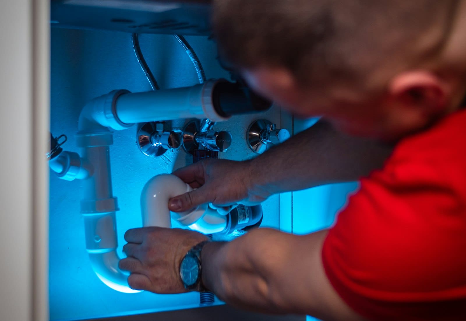 A plumber under a kitchen sink, adjusting a pipe with a wrench