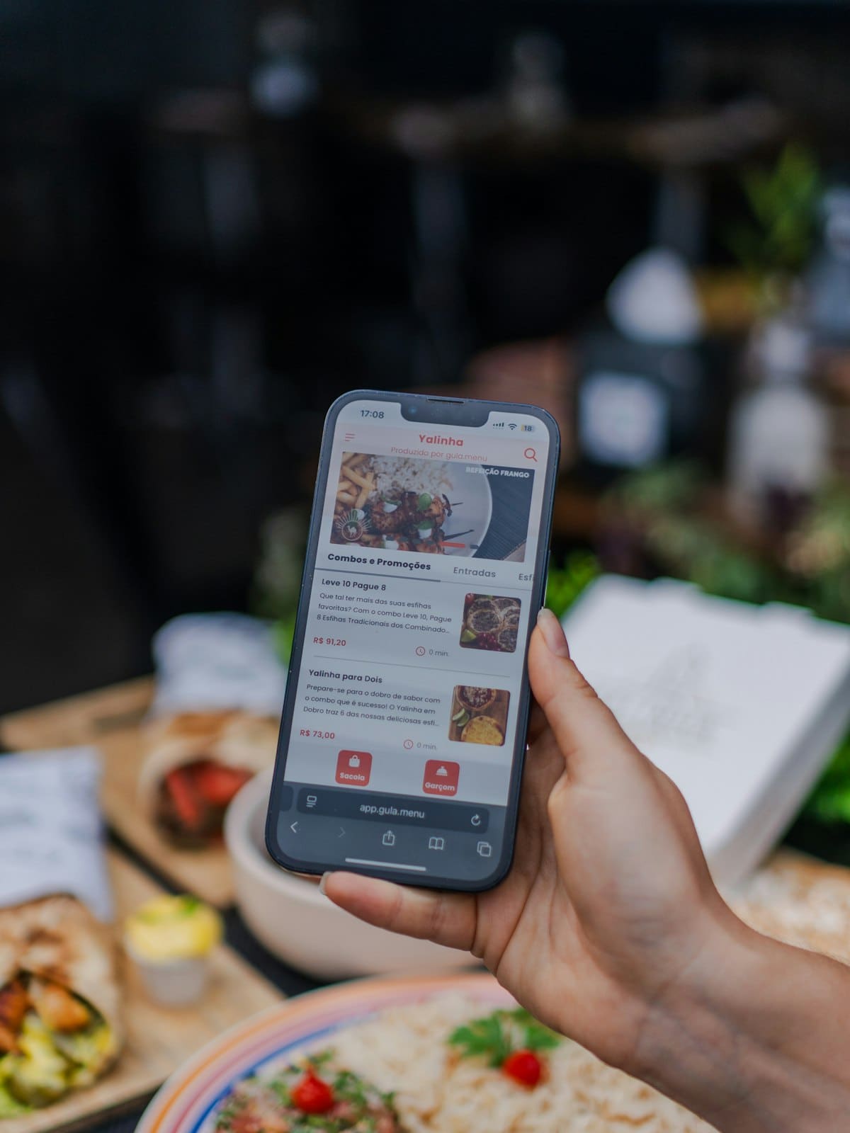 A hand holding a phone running a food ordering app at a table