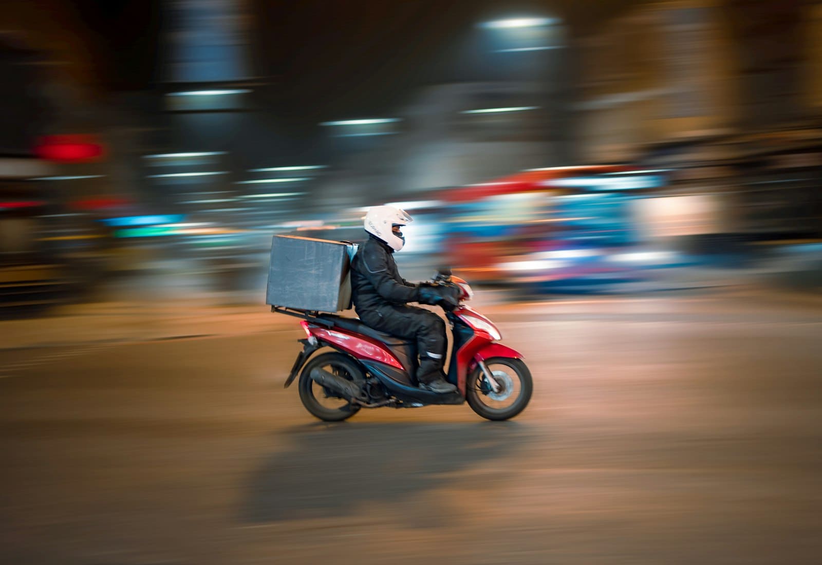 A delivery rider on a scooter moving through city traffic at night